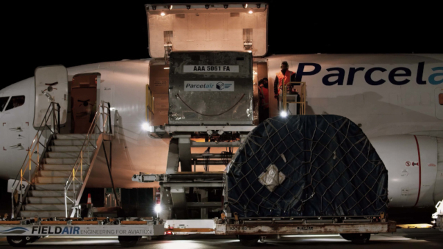 Night-time photo of a man unloading freight from a Parcelair plane at a Te Utananui airport.