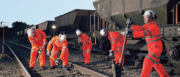 A group of railway workers in hi-vis gear and helmets working on railway tracks, sleepers and equipment