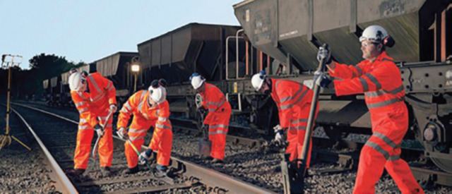 A group of railway workers in hi-vis gear and helmets working on railway tracks, sleepers and equipment
