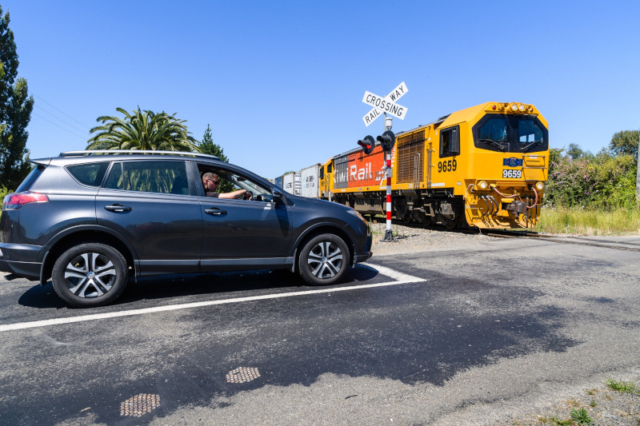 Photo of a car stopped at a level railway crossing as a KiwiRail train goes by